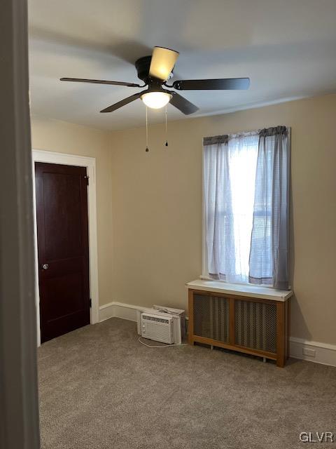 carpeted spare room with a wall unit AC, radiator, and ceiling fan