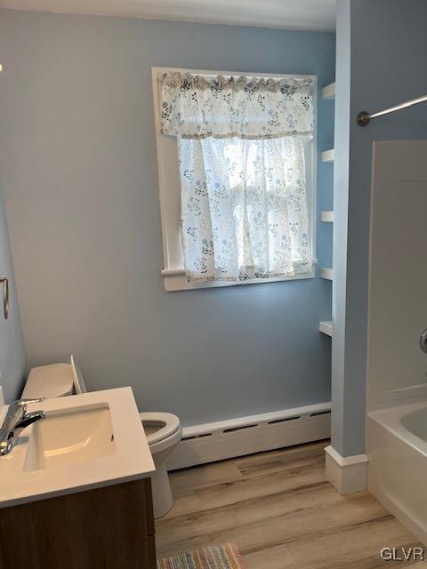 full bathroom featuring washtub / shower combination, hardwood / wood-style floors, vanity, a baseboard heating unit, and toilet