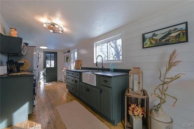 kitchen featuring a textured ceiling, wood walls, light wood-type flooring, and sink