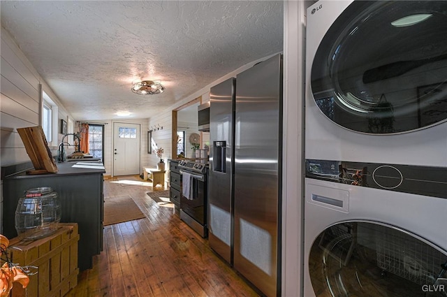 kitchen featuring a textured ceiling, dark wood-type flooring, stacked washer / drying machine, stainless steel appliances, and sink