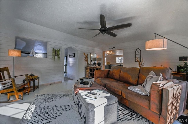 living room featuring ceiling fan, wooden walls, and a textured ceiling