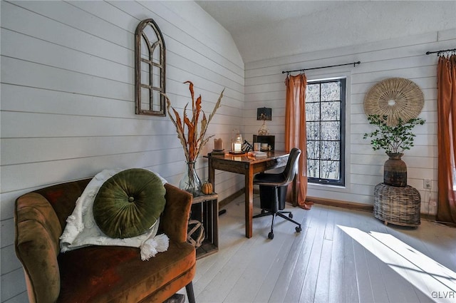 home office with light wood-type flooring, vaulted ceiling, and wooden walls