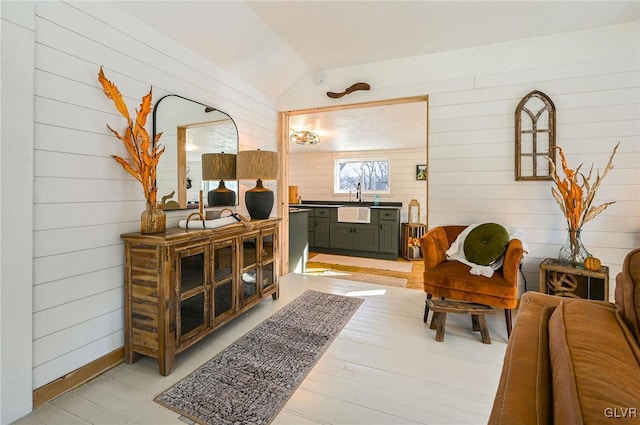 living area featuring light wood-type flooring, wood walls, and vaulted ceiling