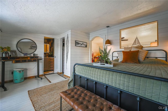 bedroom with a textured ceiling, wood walls, and hardwood / wood-style floors