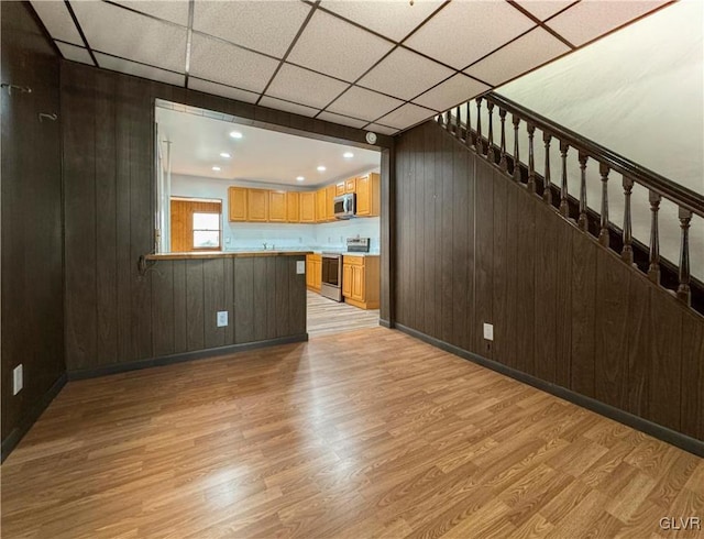 unfurnished living room with wooden walls, light hardwood / wood-style flooring, and a drop ceiling