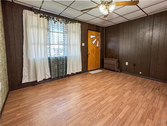 foyer entrance with wood walls, radiator, a paneled ceiling, and light wood-type flooring