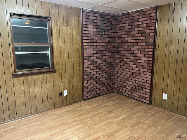 empty room featuring brick wall, wooden walls, and light hardwood / wood-style flooring