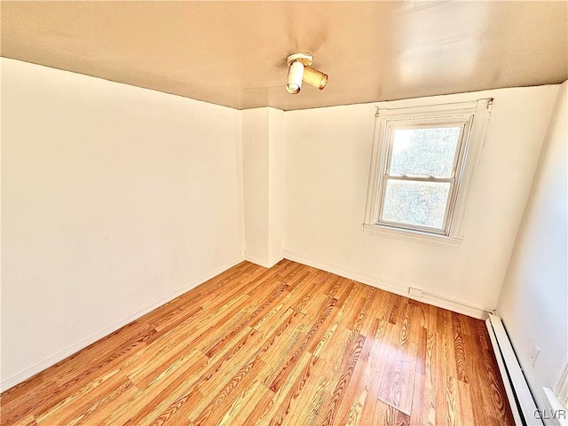 spare room featuring baseboard heating and light hardwood / wood-style floors