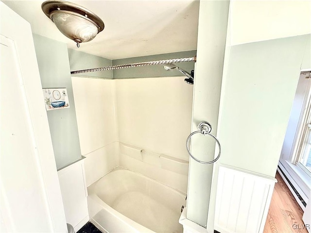 bathroom with wood-type flooring, washtub / shower combination, and a baseboard heating unit