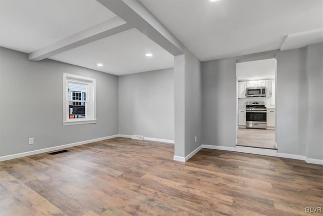 empty room featuring beamed ceiling and wood-type flooring