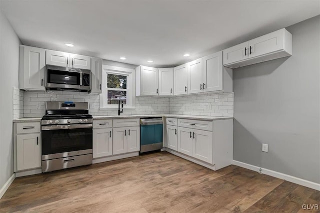 kitchen with appliances with stainless steel finishes, decorative backsplash, sink, hardwood / wood-style flooring, and white cabinets