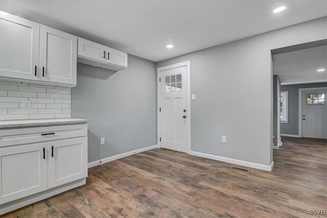 kitchen with dark hardwood / wood-style floors, white cabinetry, backsplash, and light stone counters