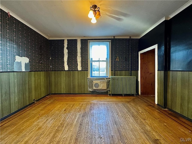 empty room with ornamental molding, radiator, ceiling fan, wood-type flooring, and wooden walls