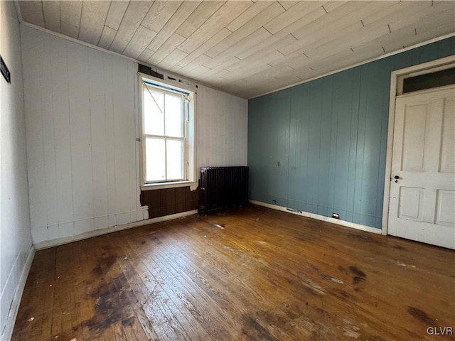 empty room featuring radiator, hardwood / wood-style floors, wooden ceiling, and wood walls