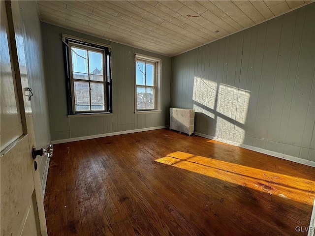 unfurnished room with wood walls, wood-type flooring, wood ceiling, and radiator