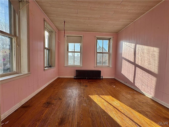 unfurnished room featuring hardwood / wood-style floors, wood walls, wooden ceiling, and radiator