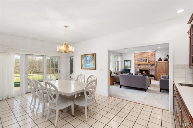 carpeted dining area with a brick fireplace, sink, and an inviting chandelier