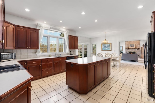 kitchen featuring sink, backsplash, a center island, a brick fireplace, and pendant lighting