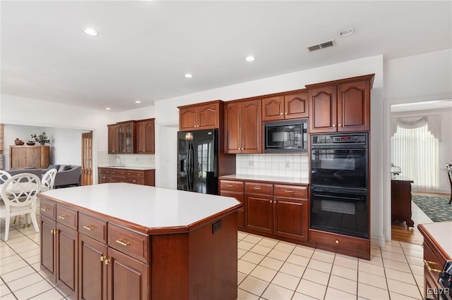 kitchen featuring decorative backsplash, light tile patterned floors, black appliances, and a kitchen island