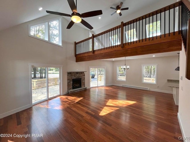 unfurnished living room with hardwood / wood-style floors, ceiling fan with notable chandelier, a stone fireplace, baseboard heating, and plenty of natural light