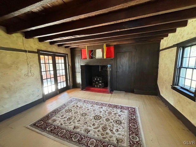 unfurnished living room featuring beamed ceiling, french doors, a high end fireplace, and light hardwood / wood-style flooring