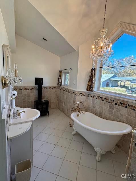 bathroom featuring a bath, tile walls, tile patterned floors, a wood stove, and a notable chandelier