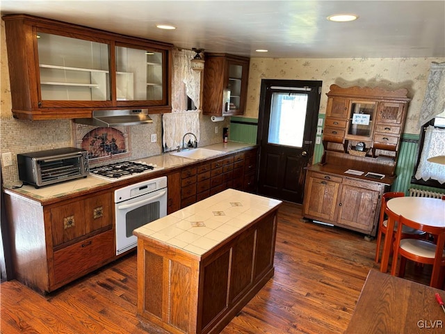 kitchen featuring tile countertops, stainless steel gas cooktop, sink, white oven, and ventilation hood