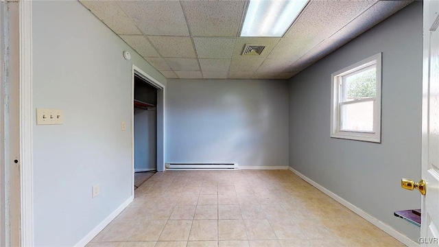 unfurnished bedroom featuring a drop ceiling, baseboard heating, and light tile patterned flooring