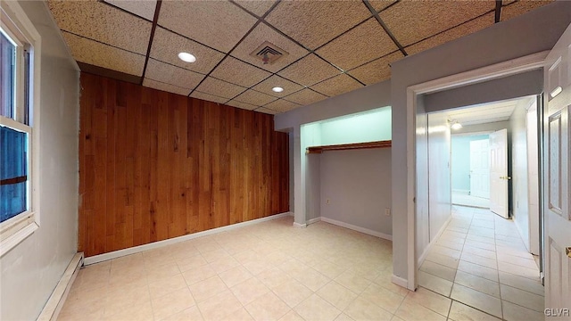 unfurnished room featuring wood walls, a baseboard heating unit, and a drop ceiling