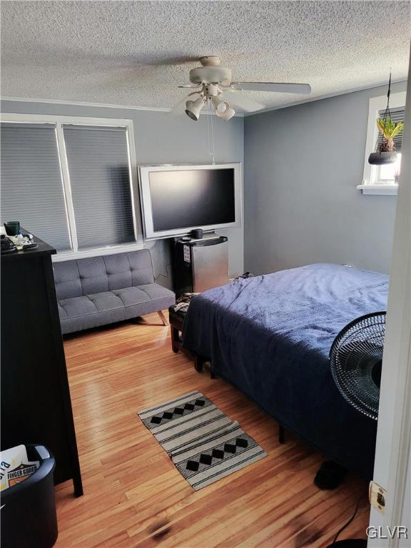 bedroom with hardwood / wood-style floors, ceiling fan, and a textured ceiling