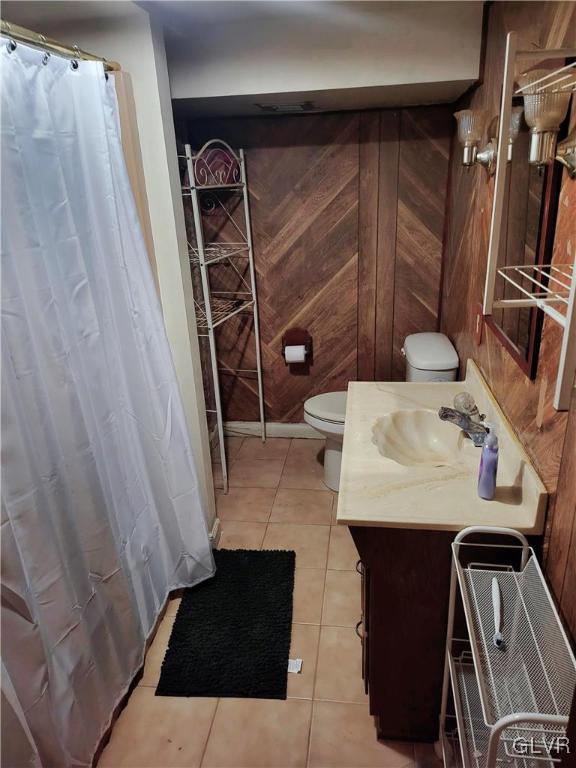 bathroom with toilet, vanity, wooden walls, and tile patterned floors