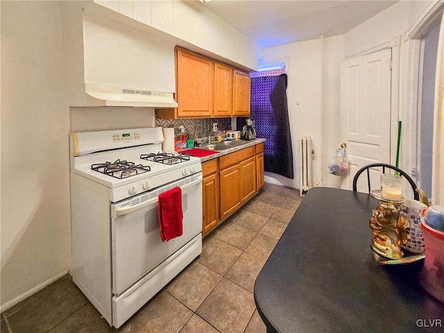 kitchen featuring radiator, range hood, white range with gas stovetop, dark tile patterned flooring, and sink