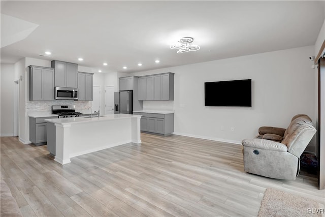 kitchen with appliances with stainless steel finishes, light hardwood / wood-style floors, gray cabinetry, and an island with sink