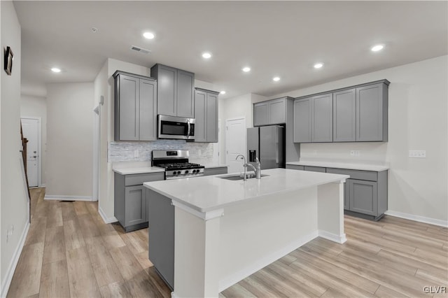 kitchen featuring gray cabinetry, sink, appliances with stainless steel finishes, and an island with sink