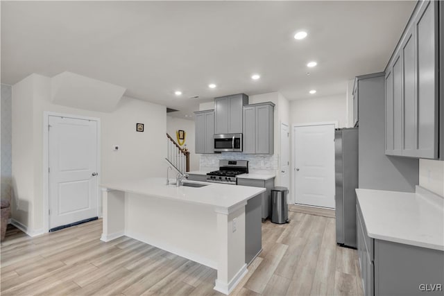 kitchen featuring a center island with sink, decorative backsplash, gray cabinets, light wood-type flooring, and stainless steel appliances