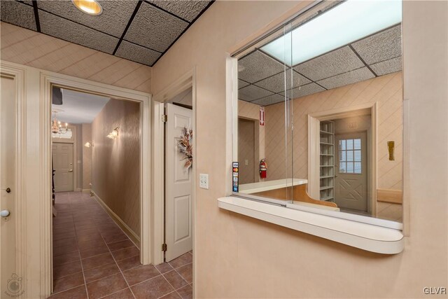 hallway featuring dark tile patterned flooring, a paneled ceiling, and a notable chandelier