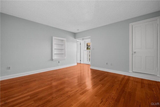 empty room featuring built in shelves, hardwood / wood-style floors, and a textured ceiling