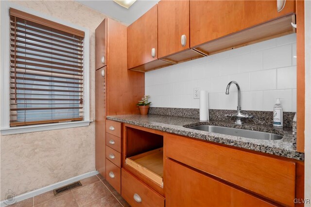 kitchen with light tile patterned floors, stone counters, sink, and backsplash