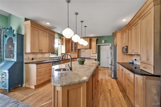 kitchen with stainless steel appliances, light hardwood / wood-style floors, sink, dark stone counters, and hanging light fixtures