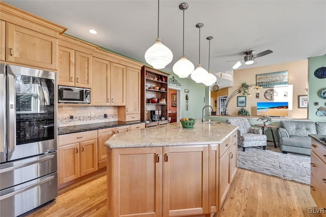 kitchen with a center island with sink, stainless steel appliances, pendant lighting, light stone countertops, and light hardwood / wood-style flooring