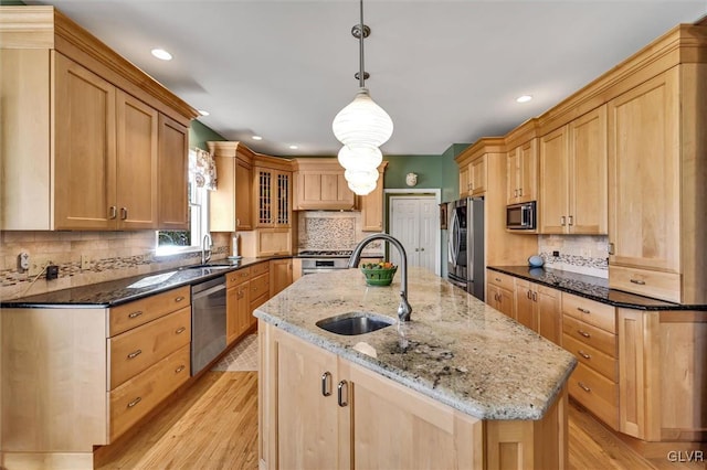 kitchen with pendant lighting, sink, light stone counters, and a center island with sink