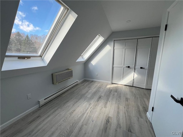 additional living space featuring lofted ceiling with skylight, a wall unit AC, light hardwood / wood-style floors, and a baseboard heating unit