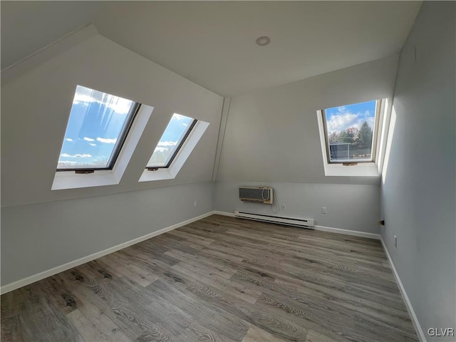 additional living space featuring lofted ceiling with skylight, a baseboard radiator, hardwood / wood-style flooring, and plenty of natural light