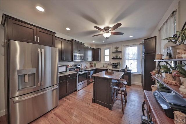 kitchen with a center island, stainless steel appliances, dark brown cabinetry, a kitchen bar, and light hardwood / wood-style flooring