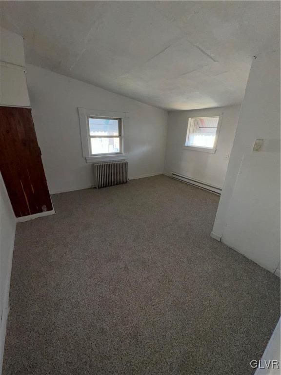 unfurnished room with radiator, dark carpet, a healthy amount of sunlight, and a baseboard heating unit