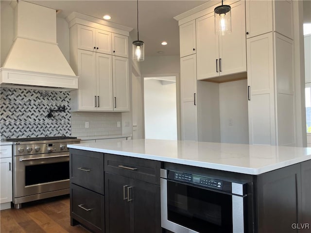 kitchen with premium range hood, appliances with stainless steel finishes, decorative light fixtures, dark hardwood / wood-style floors, and white cabinets