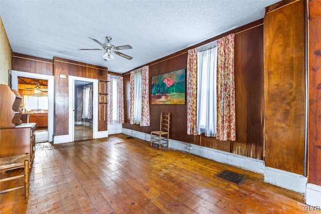 interior space with ceiling fan, french doors, wood walls, hardwood / wood-style floors, and a textured ceiling