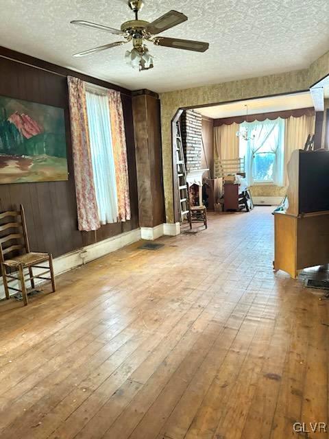 living area featuring ceiling fan, wood walls, a textured ceiling, and light wood-type flooring