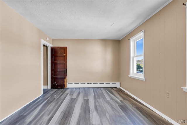 empty room with a textured ceiling, a baseboard heating unit, and hardwood / wood-style flooring