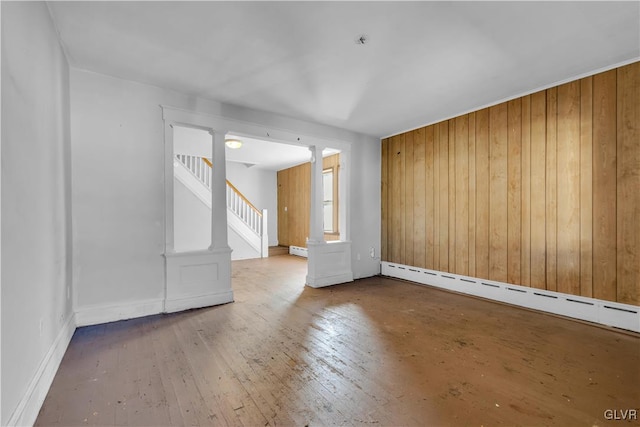 spare room featuring hardwood / wood-style floors, wood walls, decorative columns, and a baseboard radiator